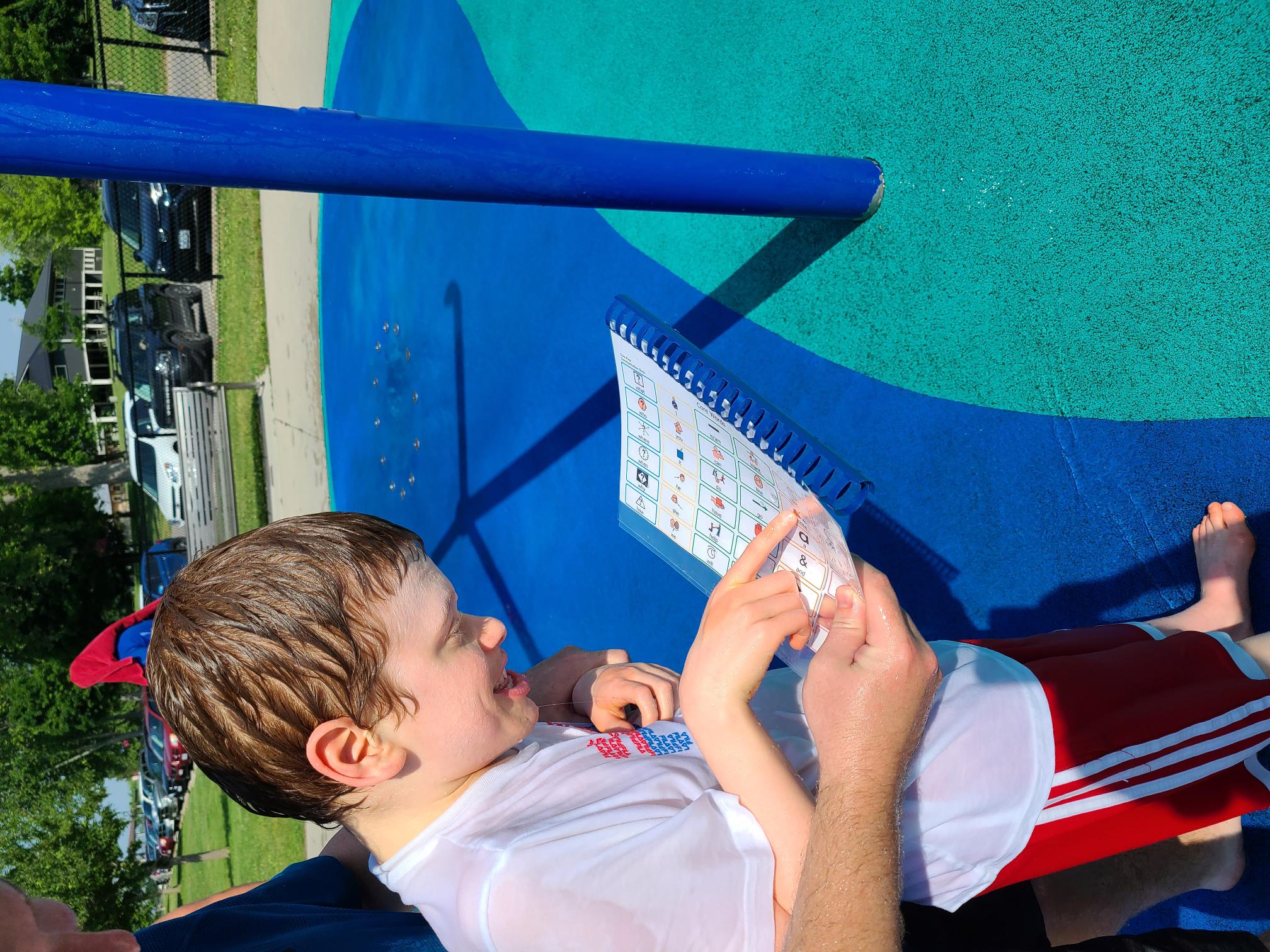 boy at splash pad with low tech communication book