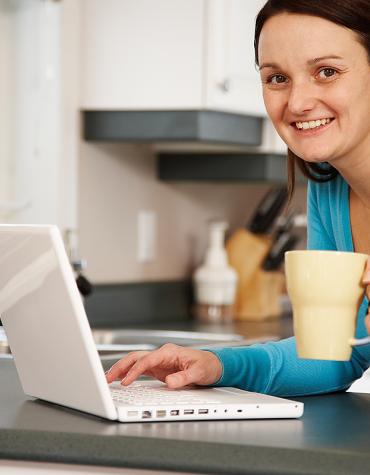 A smiling parent sitting at her computer with a mug