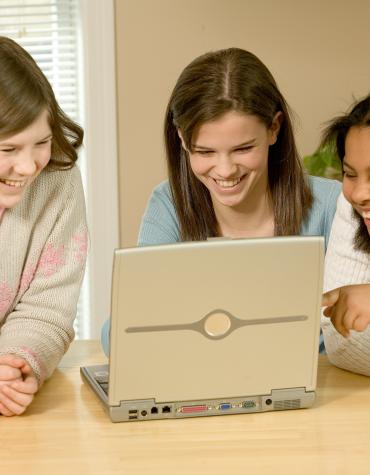 Teens around laptop playing game