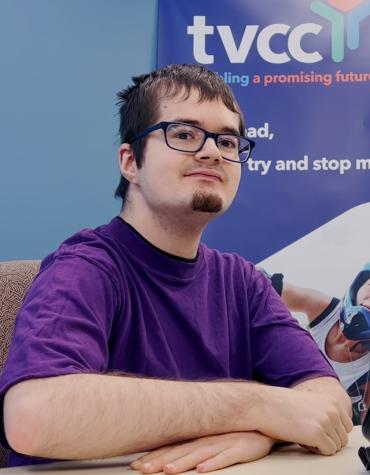 Jeremy sitting and smiling in front of a TVCC banner