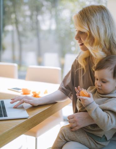 Parent sitting at table on laptop with child on their lap