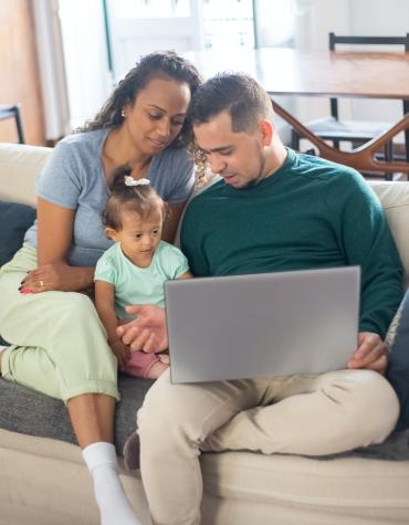 Parents and child sitting on couch looking at computer