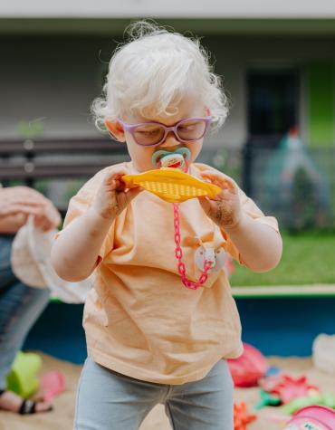 Toddler with glasses standing and looking at a toy