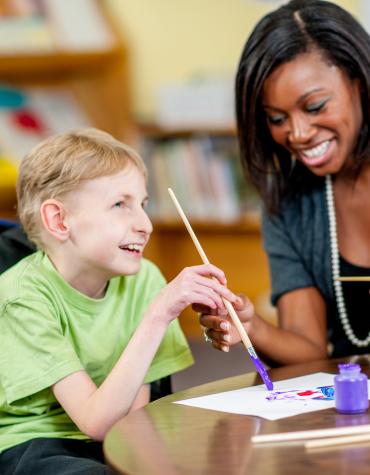 child in wheelchair painting a picture with adult