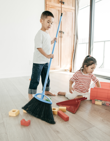 Child sweeping up toys and another child picking up blocks