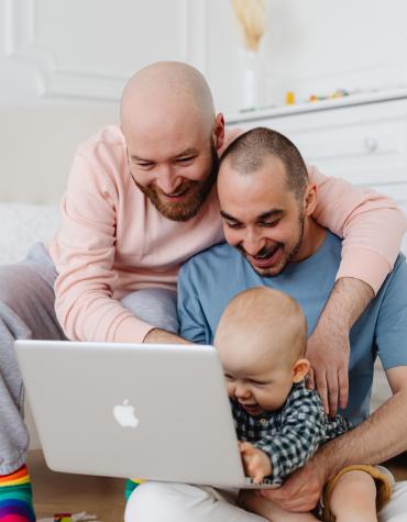 Two adults hugging and holding baby while looking at a laptop