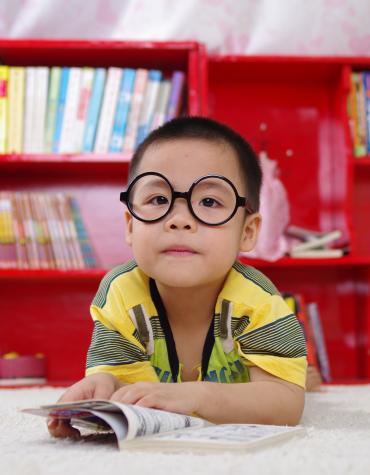 Young child wearing glasses laying on stomach reading a book