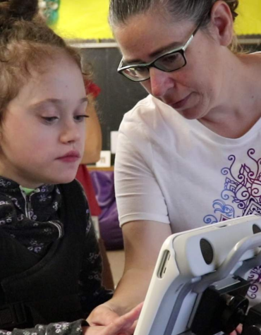 Child using augmentative communciation device with help from adult