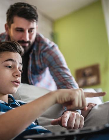 teen with dad , wearing headphones and using a laptop