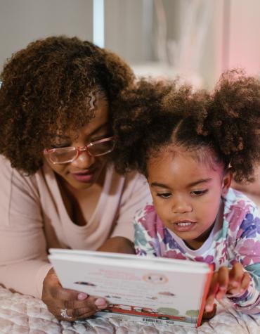 Adult and child laying on bed reading a book together