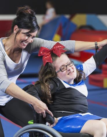 Adult helping youth in a wheelchair with gymnastic routine