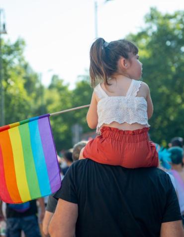child holding rainbow flag on adults shoulders